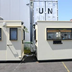Two guard shacks with bullet resistant windows and doors near UN containers